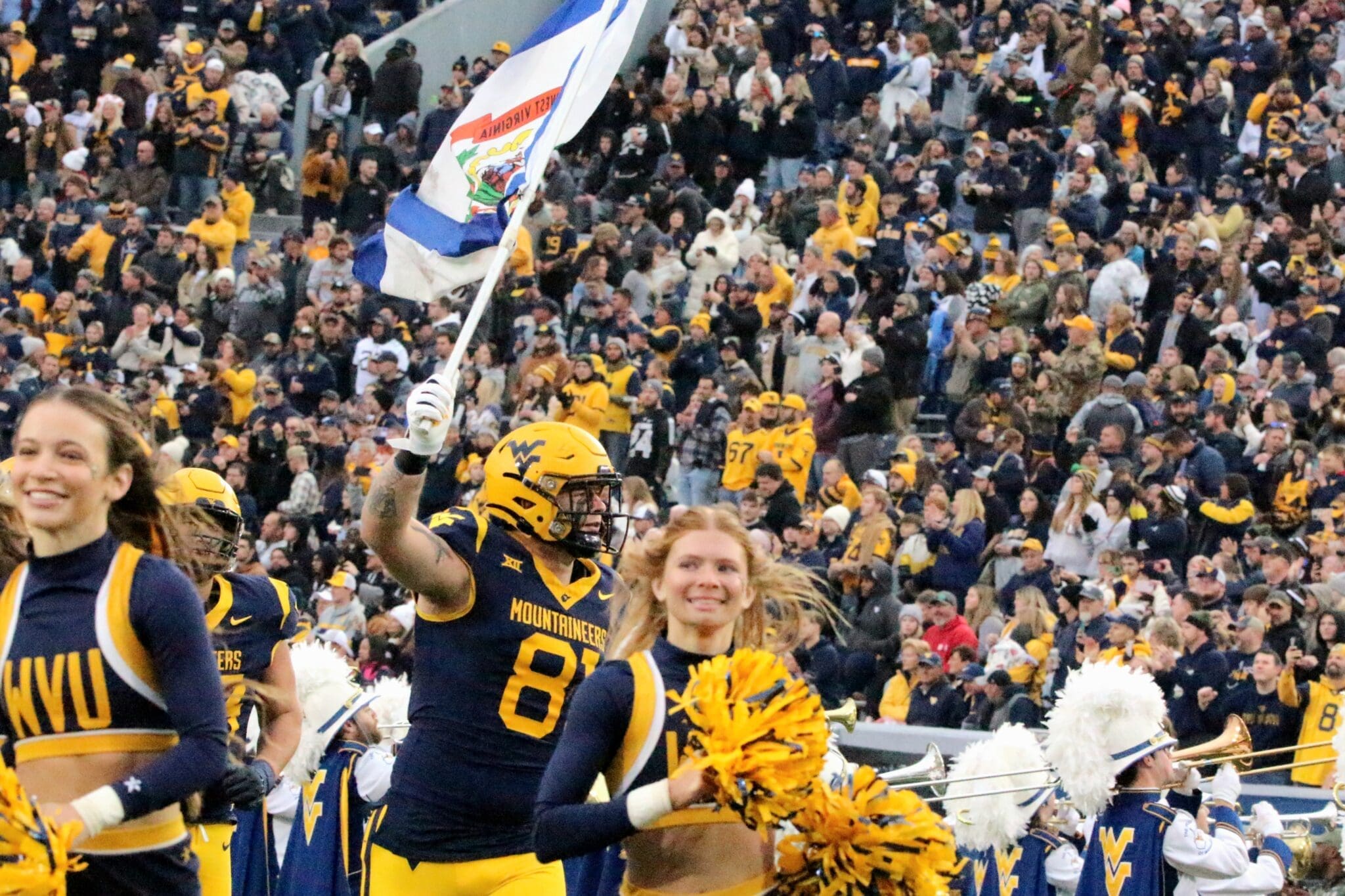 WVU Football TE Treylan Davis with WV flag and cheerleaders