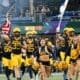 WVU Football team with US and WV flag and cheerleaders
