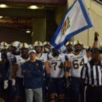WVU Football HC Neal Brown with OL and Wyatt Milan carrying flag